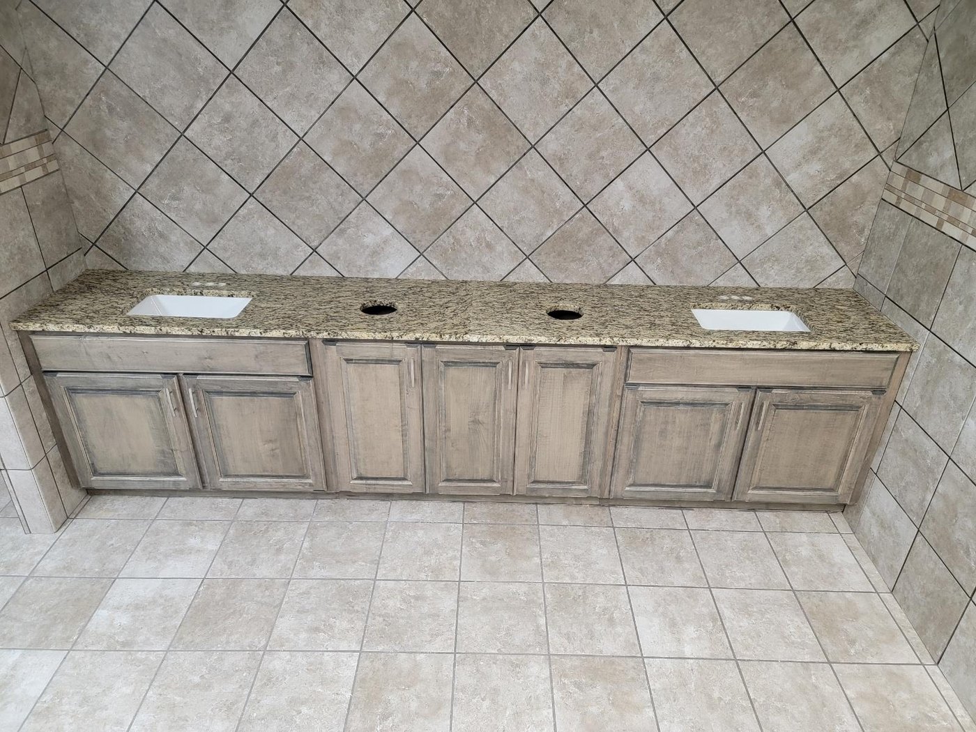 Long double vanity counter in tan and cream speckled stone with two rectangular undermount basins, over grey-washed cabinetry in a tiled bathroom