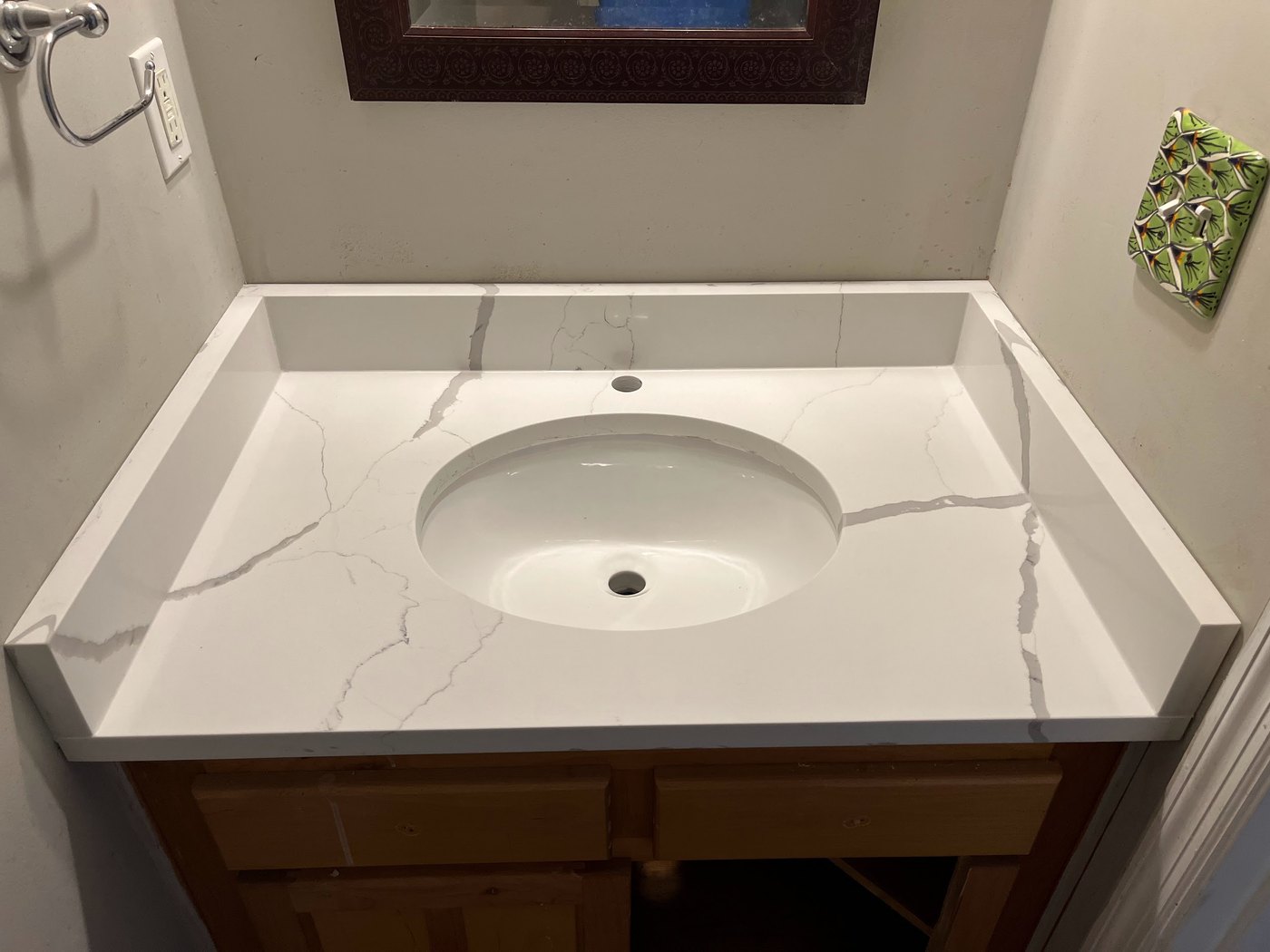 White vanity top with soft grey veining, an oval undermount basin and integral splashes returned up three sides, set on a wood cabinet