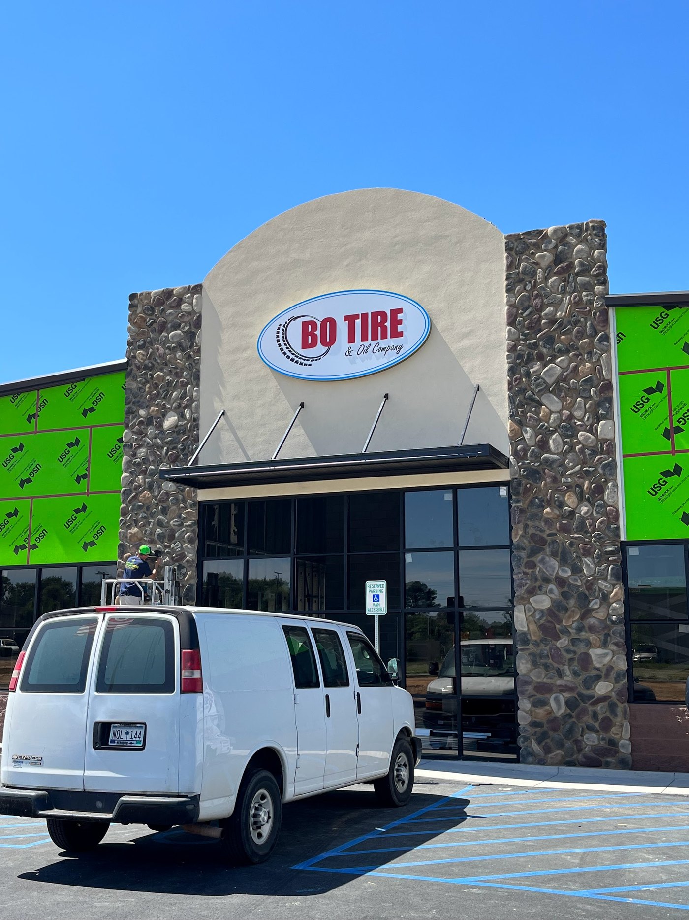 Retail storefront under construction: river-rock stone columns either side of an arched stucco entry, black awning, glass front and a work van at the kerb