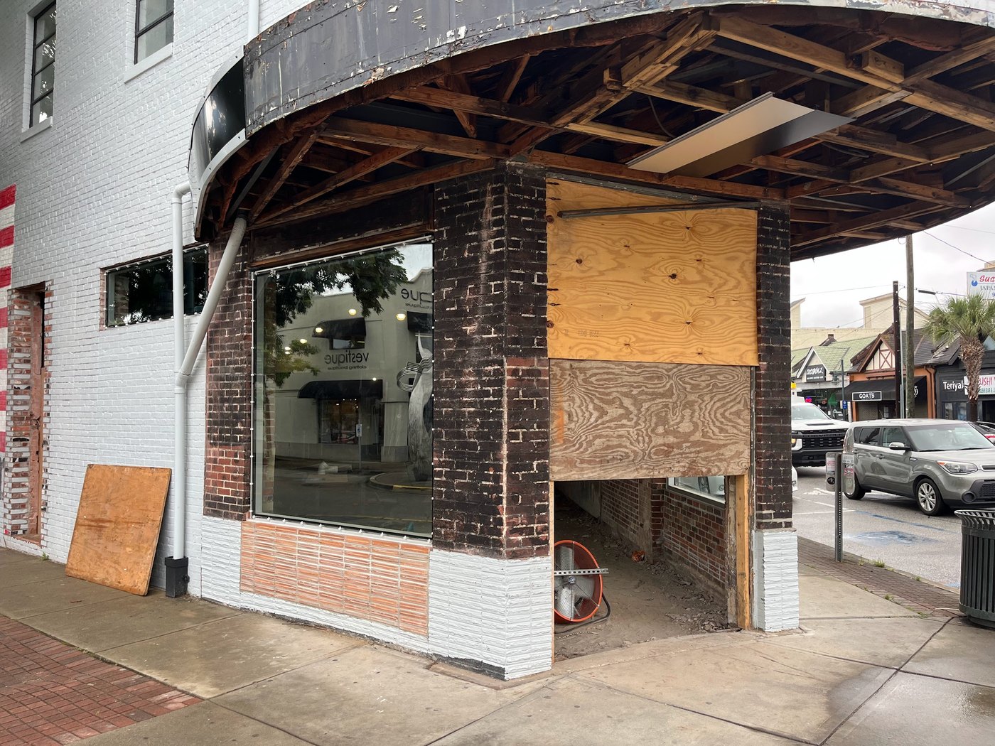 Downtown corner storefront mid-renovation, brick columns carrying a curved timber canopy over a white-painted brick facade, windows boarded with plywood