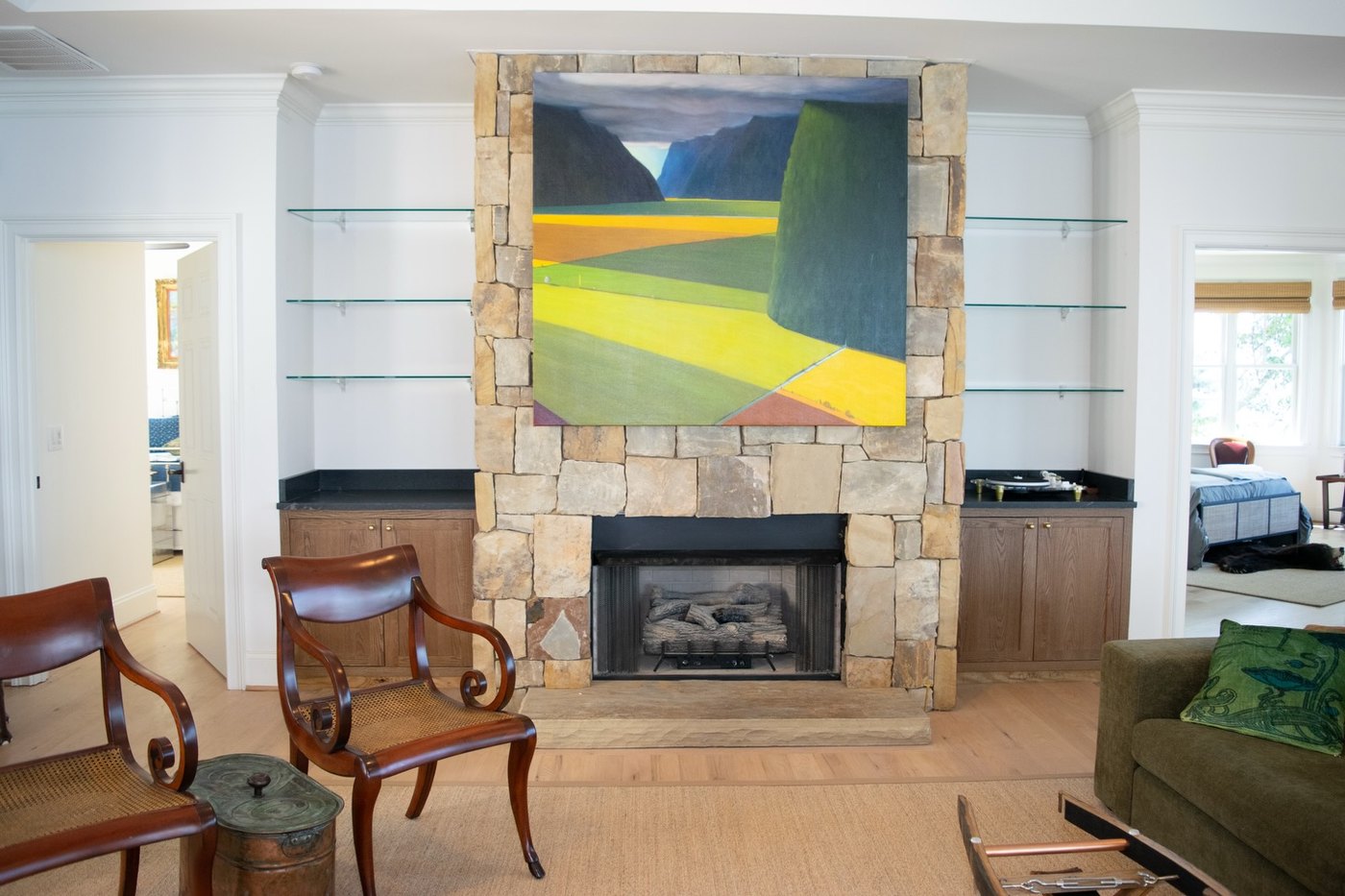 Fieldstone fireplace wall rising to the ceiling between glass display shelves and low cabinets with dark stone tops