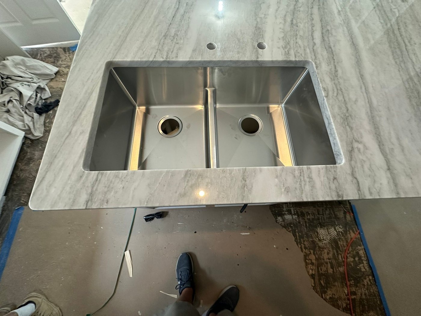 Grey-veined counter with a stainless undermount double sink, photographed from above on install day with the floor still covered