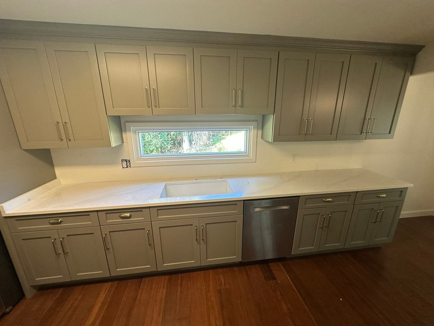 Long white counter with a sink cutout on greige cabinets, photographed before the sink and faucet went in