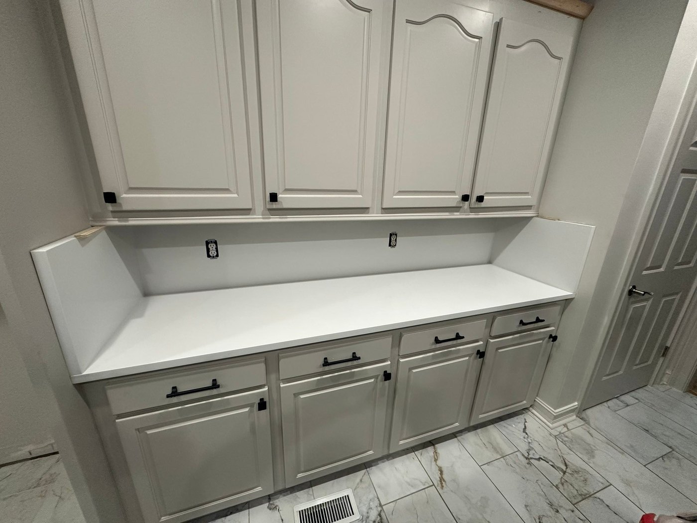 White counter on white cabinets with an upper shelf run, over a marble-look tile floor in a house under construction