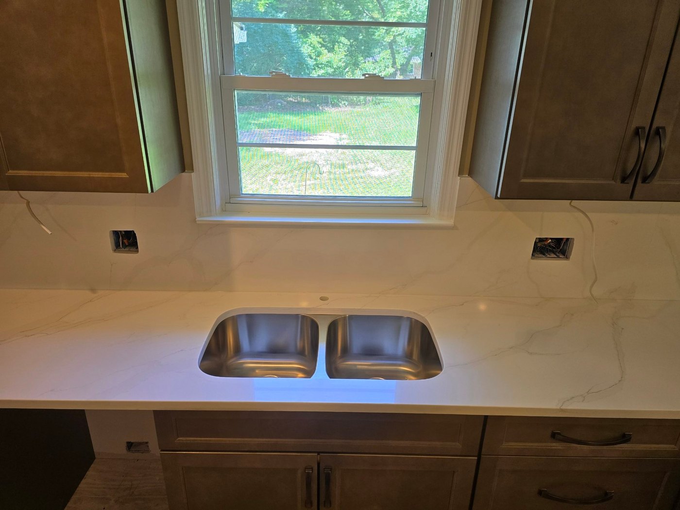 White veined counter and full-height backsplash around a window, with a stainless undermount double sink and wood cabinetry