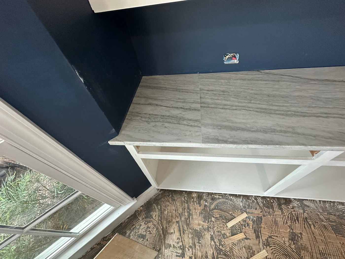 Grey-veined stone top on a white built-in cabinet against a navy wall, in a room with the subfloor still exposed