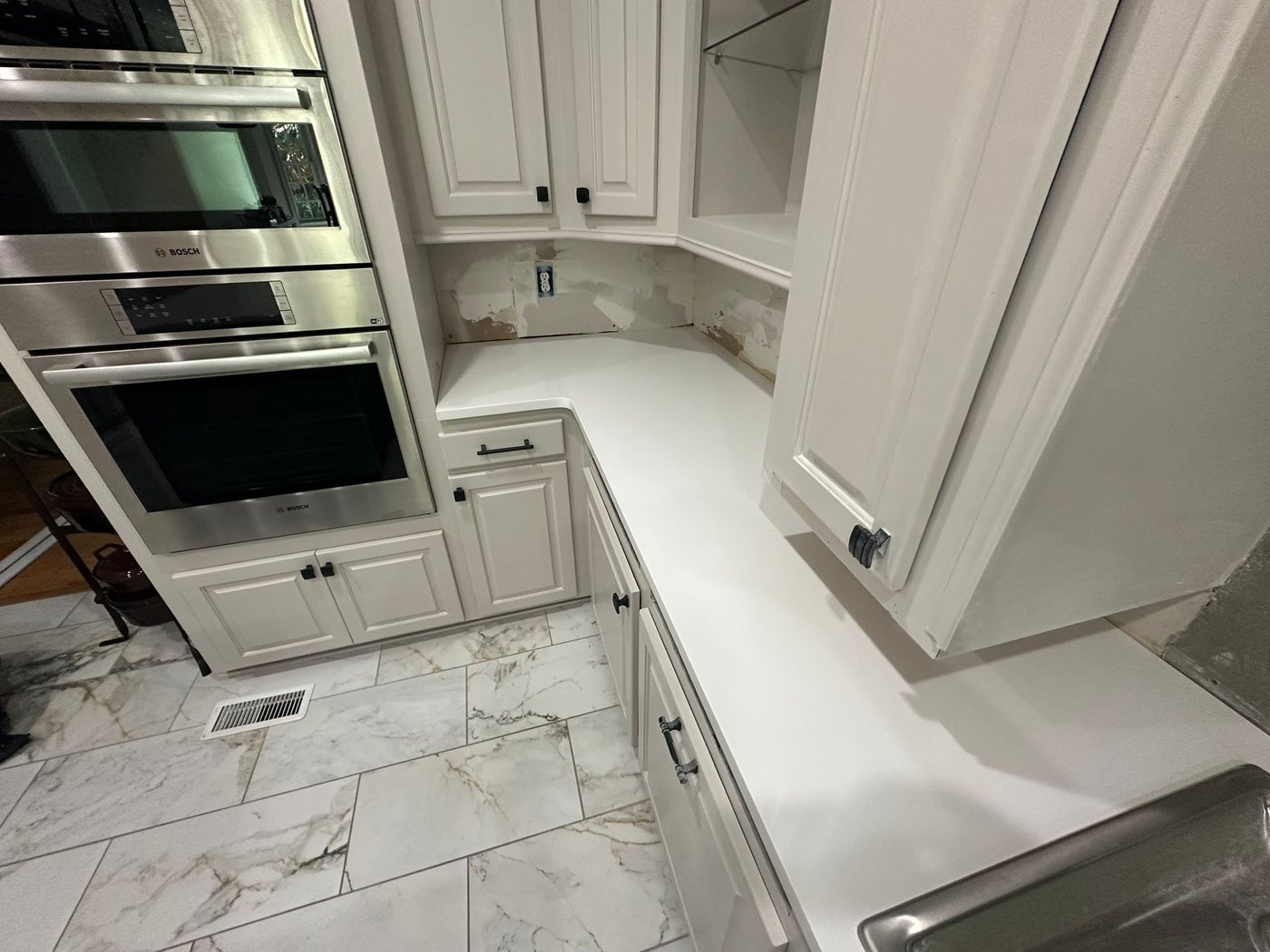 White counters wrapping a corner beside stainless wall ovens in a kitchen still being finished