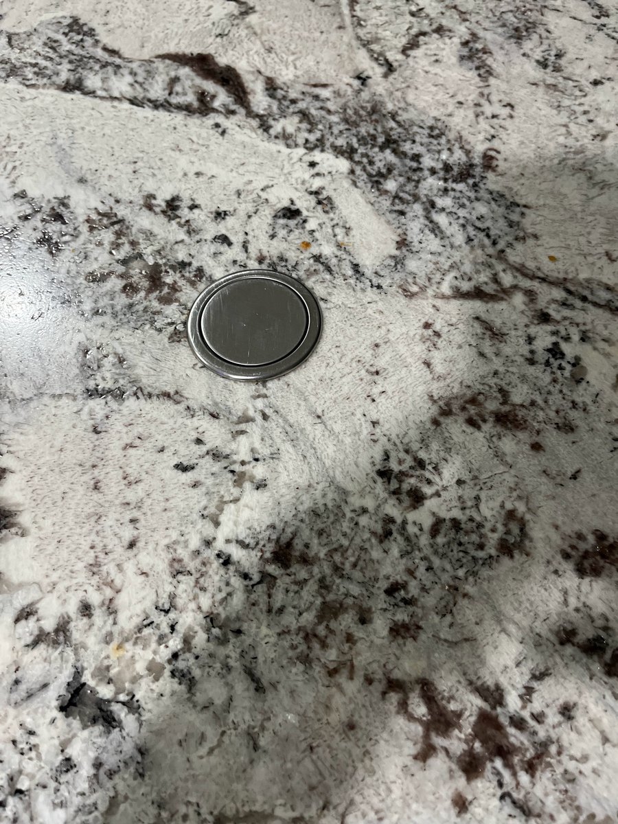 Close view of white granite with dark burgundy and black veining around a closed pop-up power outlet cap set into the surface