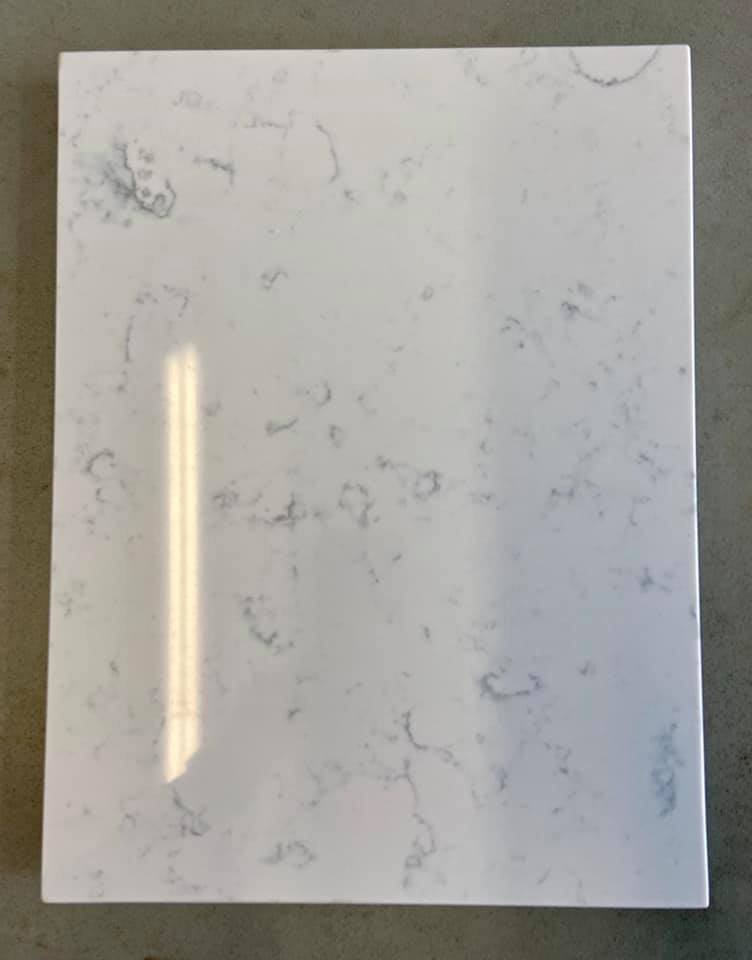 Pale gray-veined stone sample photographed flat, corner and edge visible against a concrete floor