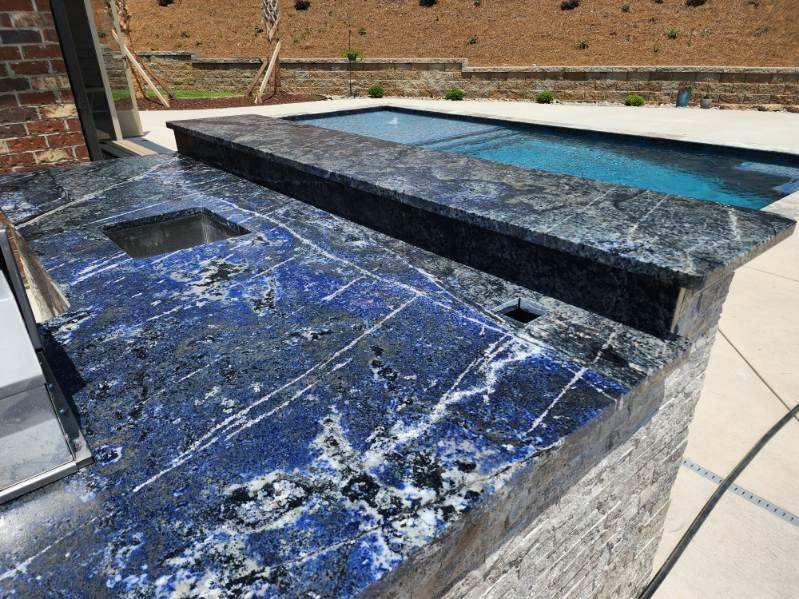Deep blue and white veined stone bar top beside a pool, wrapping the raised edge of an adjoining spa over a stacked-stone base