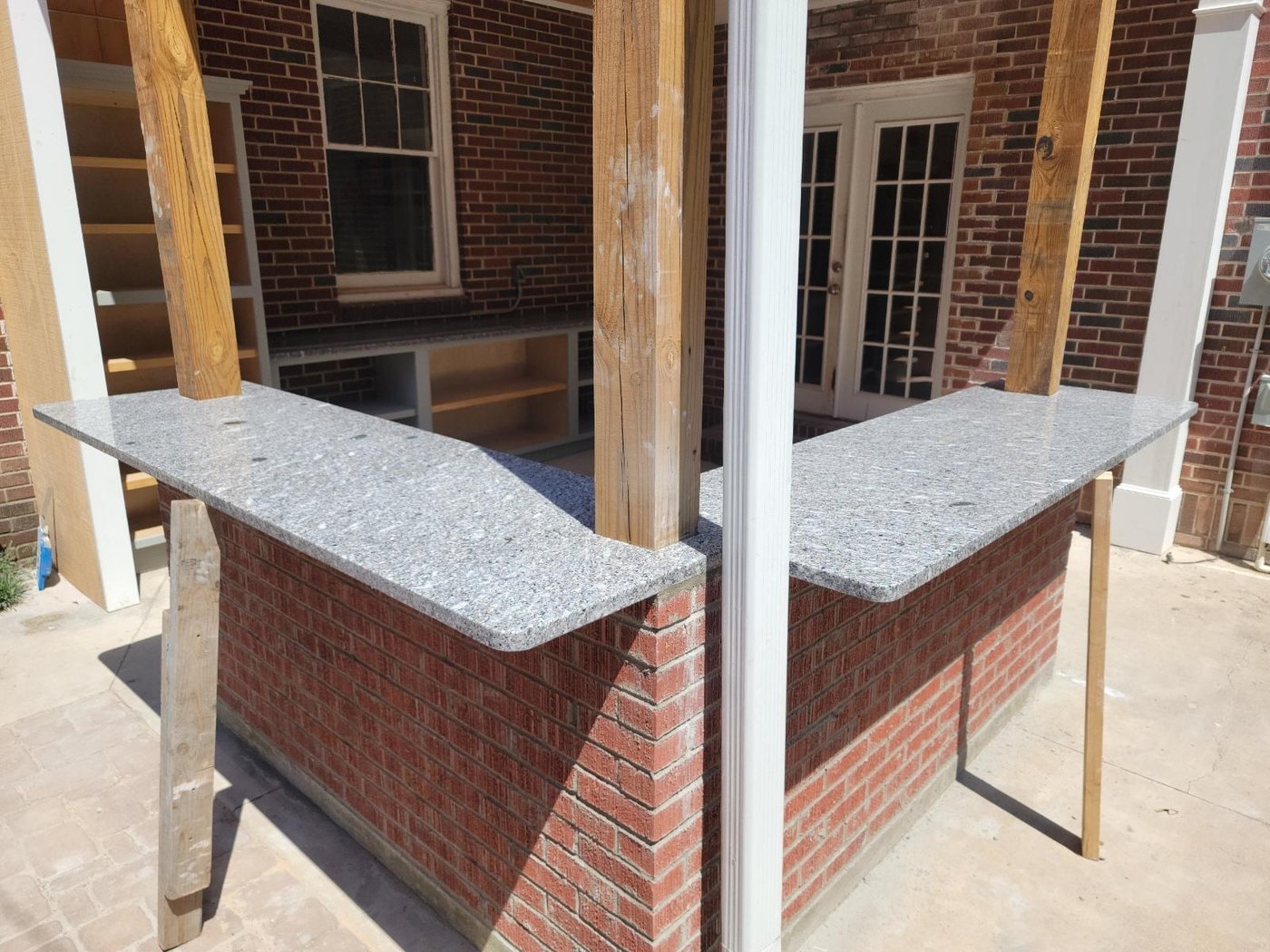 L-shaped outdoor bar with a brick base and grey speckled stone bar tops with rounded ends, under a covered porch with timber posts