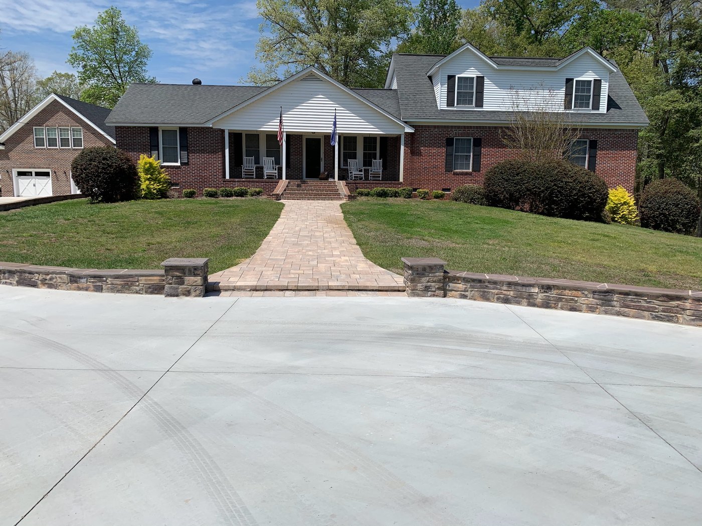 Brick ranch house with a paver walkway running from a concrete driveway up the lawn to the front porch, between low stone retaining walls with capped pillars