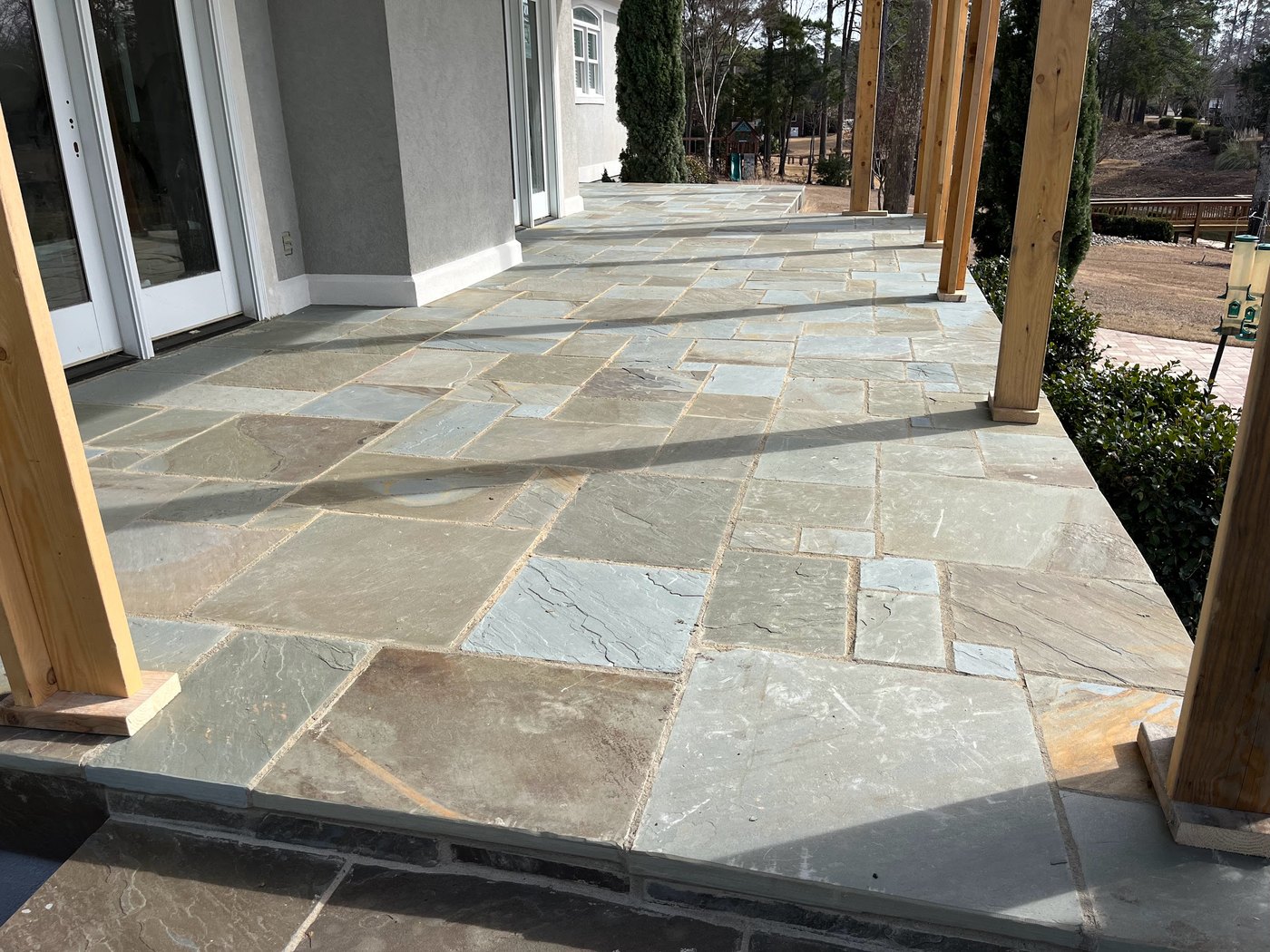 Covered flagstone porch running the length of a stucco house, laid in a random rectangular pattern with mortared joints, under timber posts