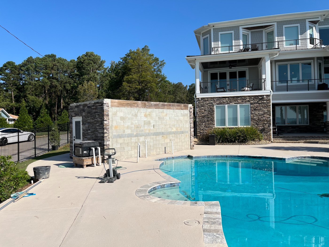 Swimming pool with a sunken spa and banded stone coping, beside a pool house faced in stacked stone, with a lakeside home behind