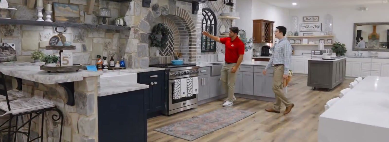 Showroom floor with a stacked-stone bar counter in the foreground and a stone arch built over a range behind it, two men in conversation beside the display