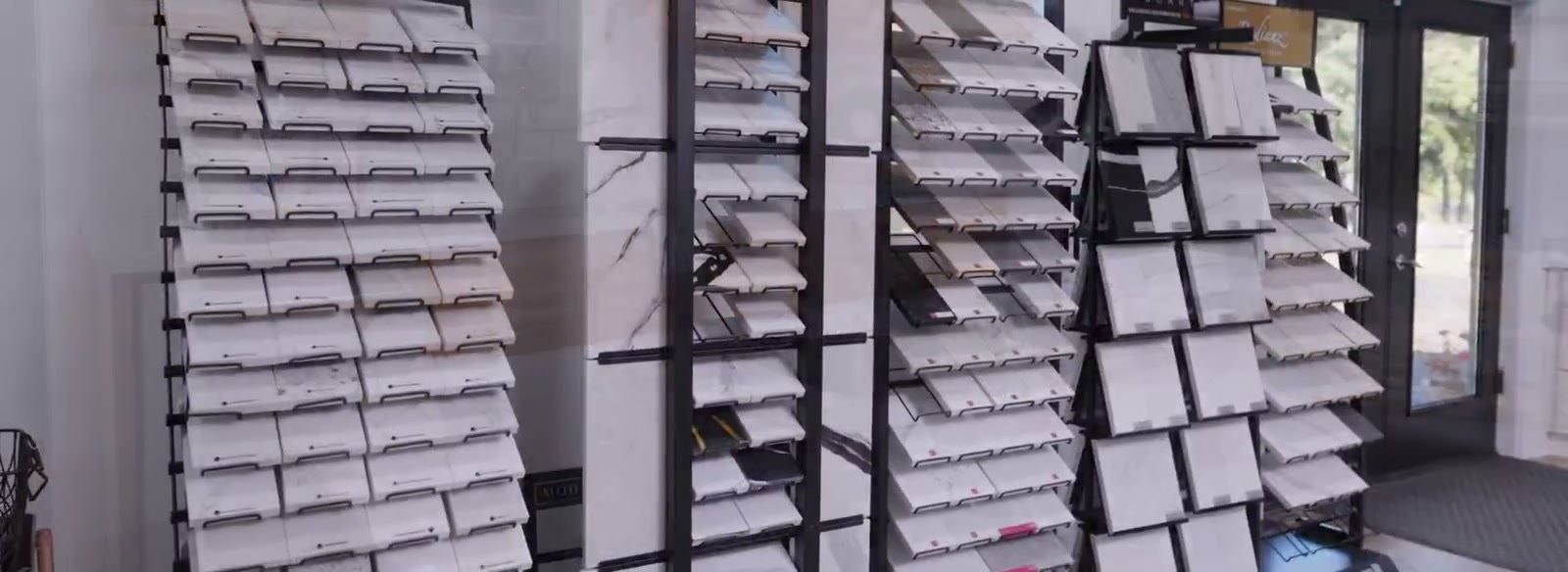 Covered sample gallery: tall black racks holding rows of stone sample boards, glass door to the outside at the right