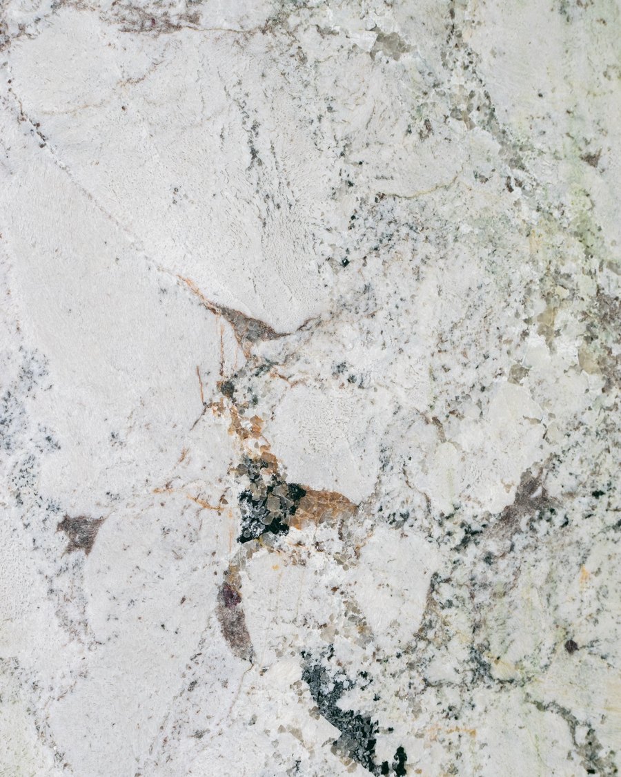Close view of a pale slab surface with grey and rust veining and clusters of dark green and black mineral