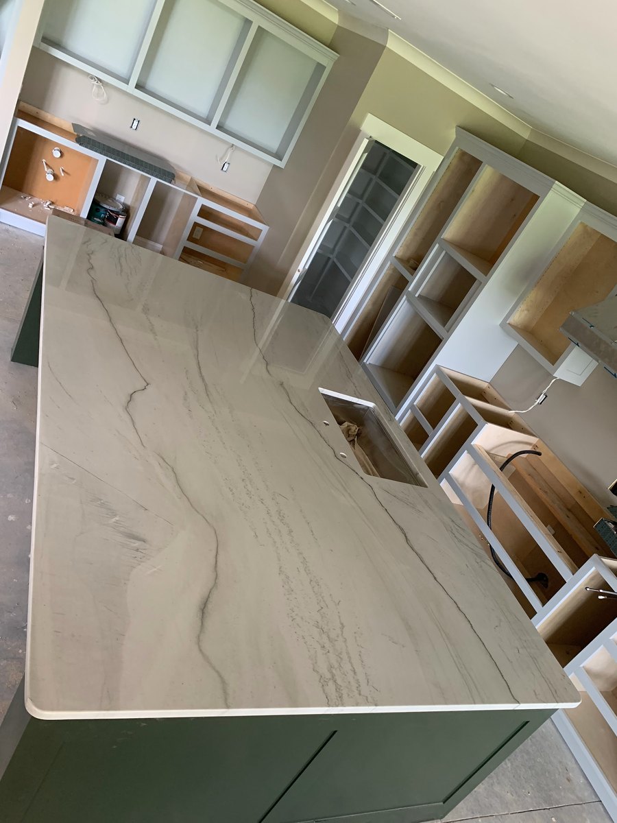 A large veined slab top set on a kitchen island in a house still under construction, with unfinished cabinetry behind